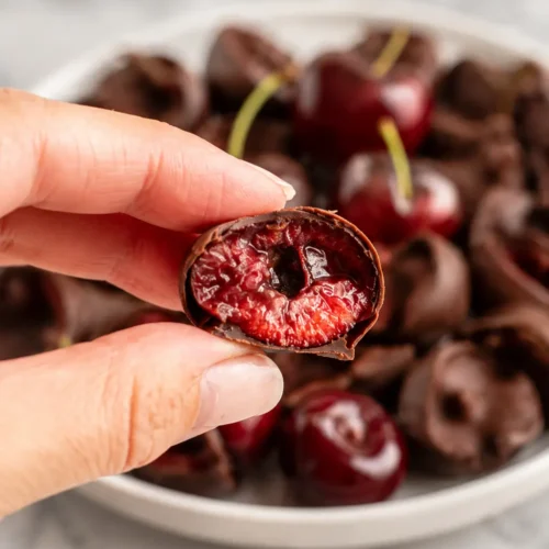 Hand holding a Chocolate-Covered Cherry with juicy red cherry center
