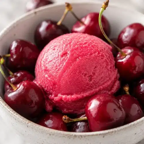 Fresh cherry sorbet scoop surrounded by ripe cherries in a rustic bowl